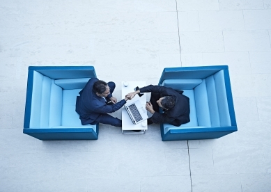 Two business men in blue chairs shaking hands